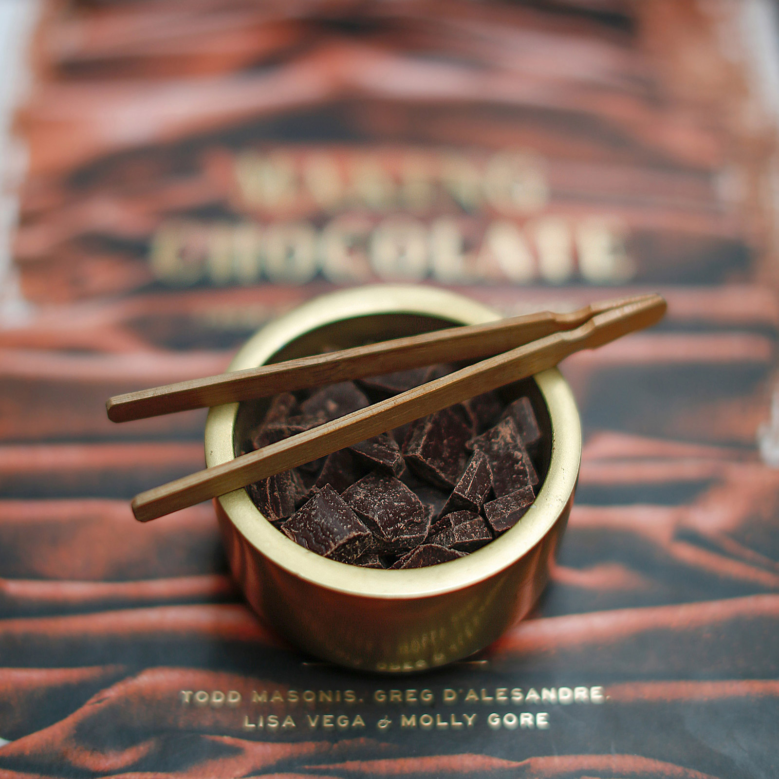 close up chocolate in gold case with wooden tweezer
