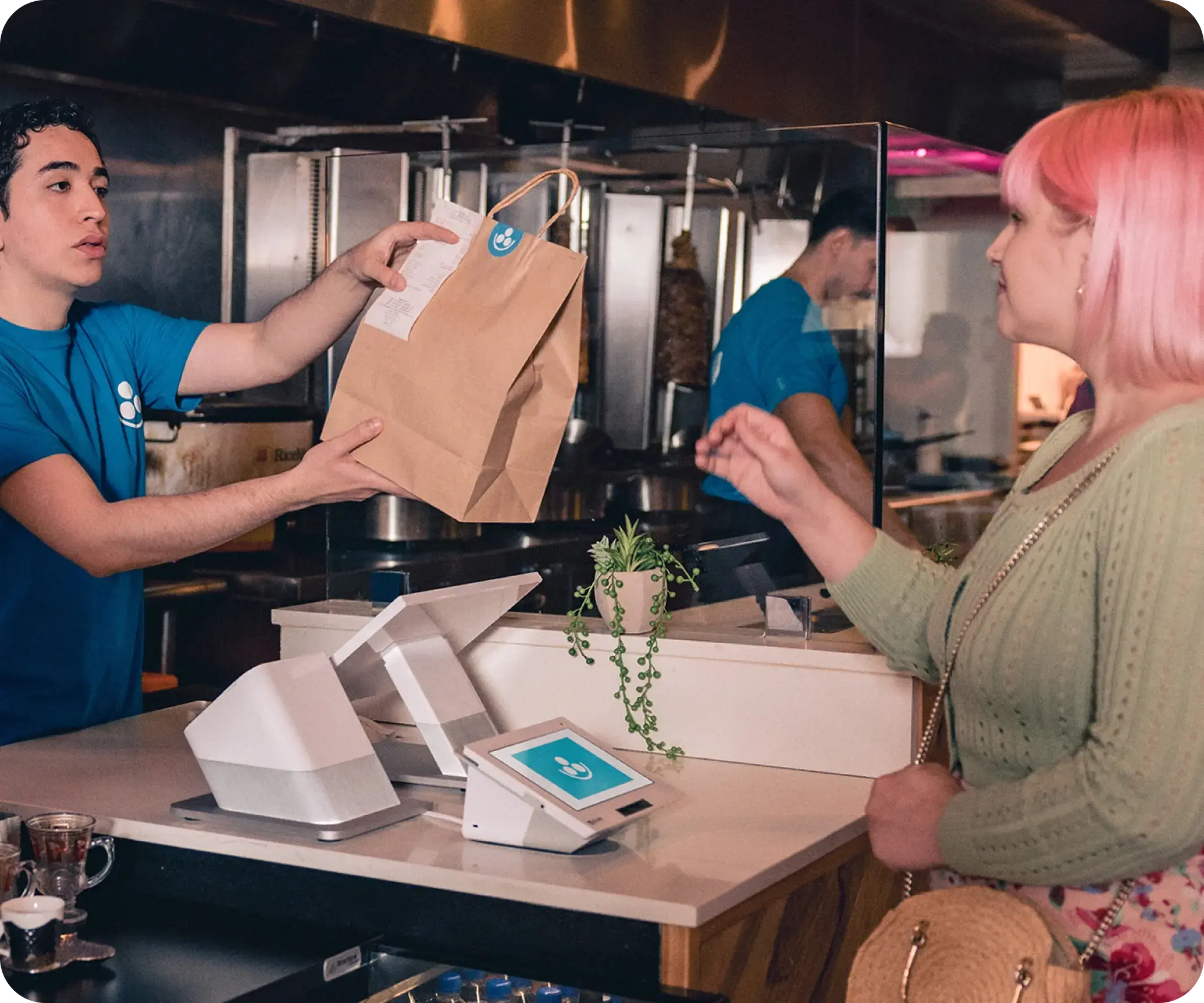 A restaurant employee hands customer a take out bag as she checks out. A Clover Station Duo device is used for payments.