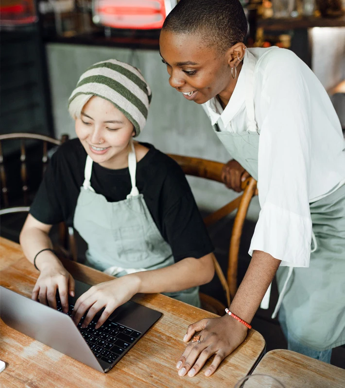 Woman sitting in front of laptop talks with a colleague who is standing beside her