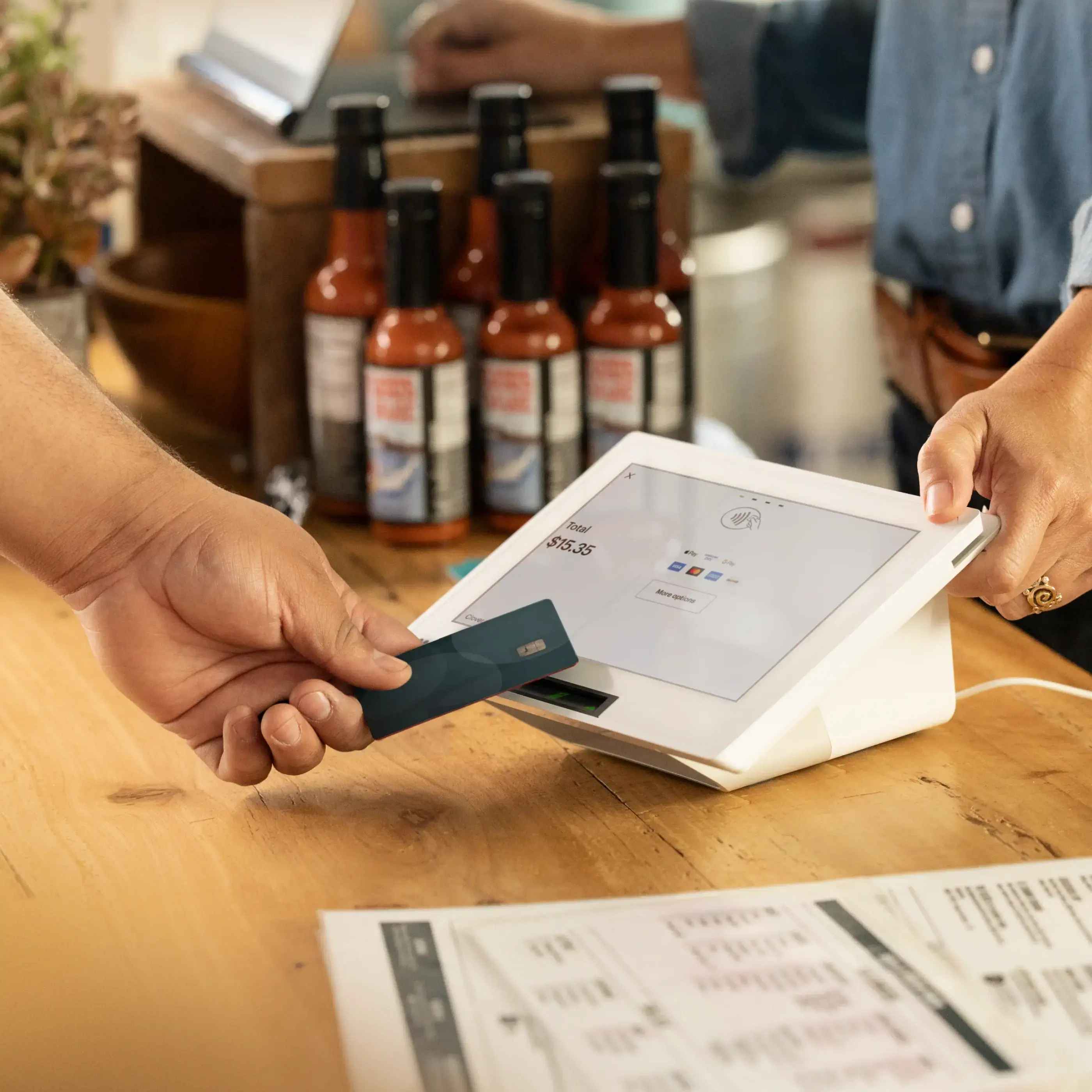 Customer tapping their credit card on a mini device in a restaurant while the merchant places their hand on the device.