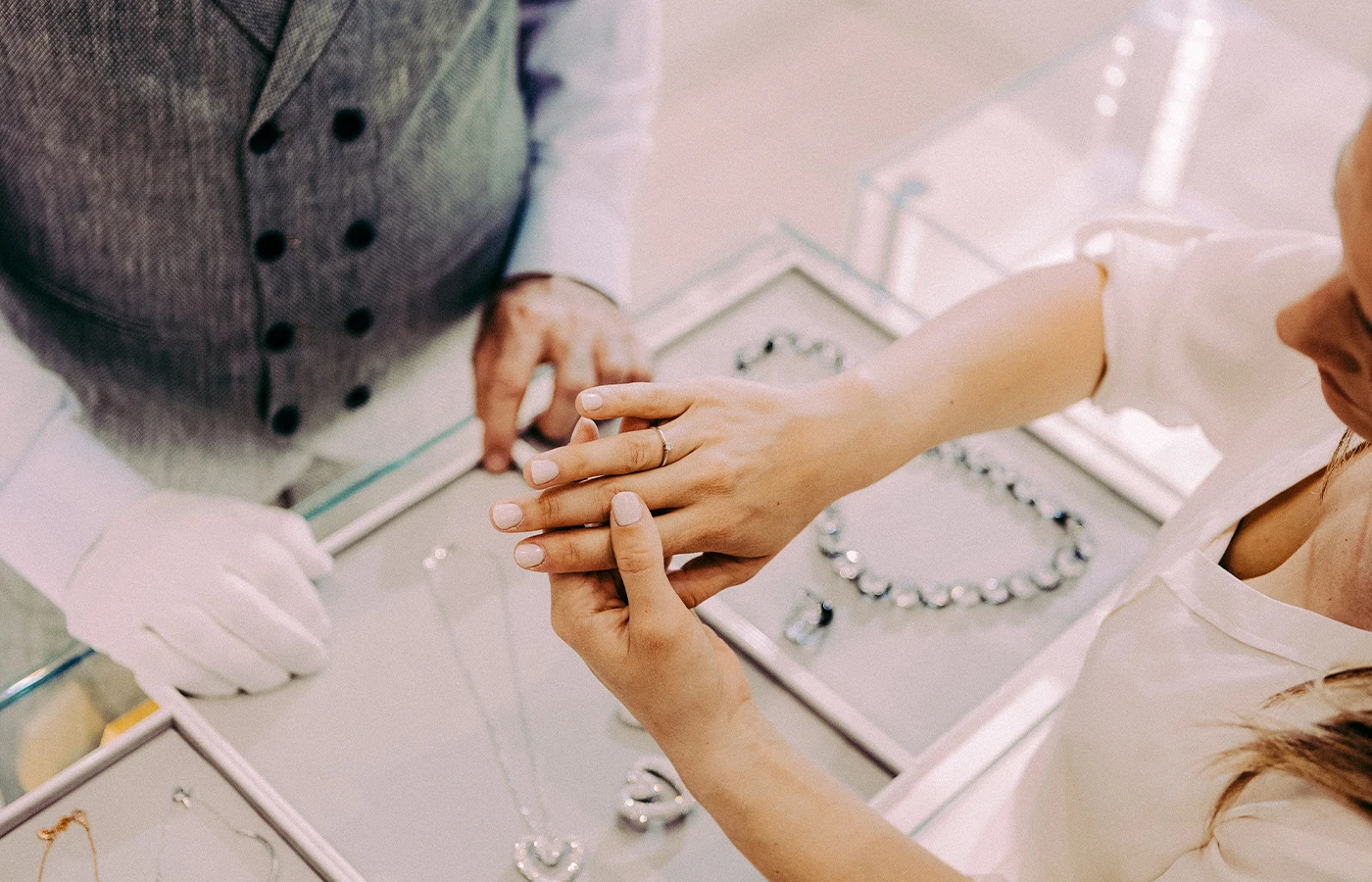 Jewelry store attendant assists woman trying on a ring.
