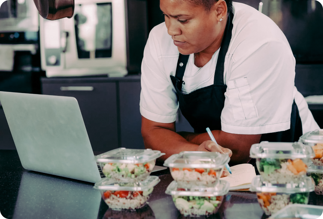Woman at the counter with a laptop writing something in a notepad