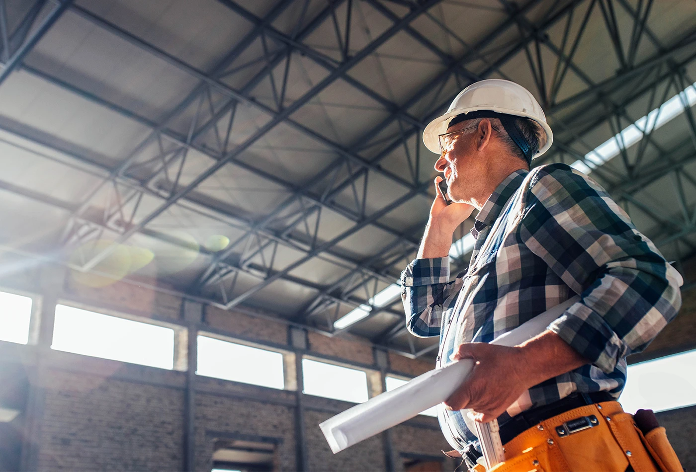 Worker on site takes a phone call whilst holding a rolled plan document.