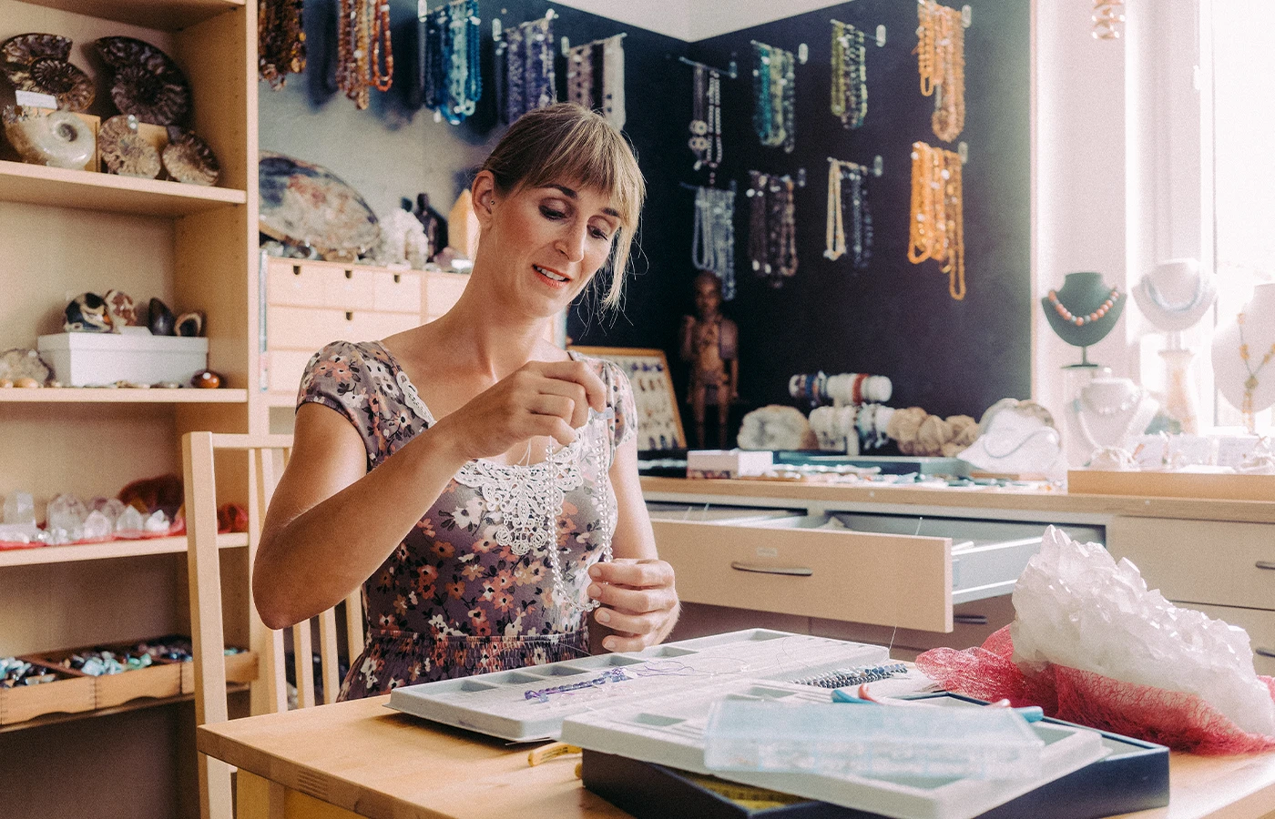 Woman sitting down in jewelry store holds up a beaded necklace.