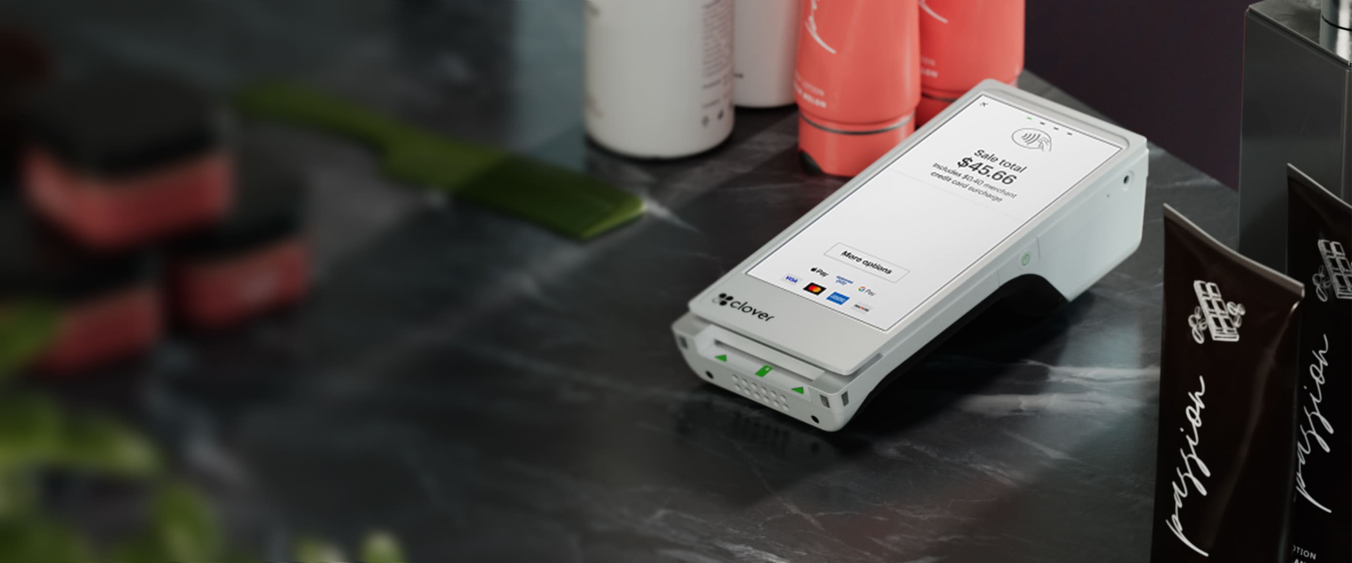 Clover flex device of white color is placed on the counter with amount to be paid is shown. A comb is kept on the table which is partially blurred and along with that few more salon products are kept.