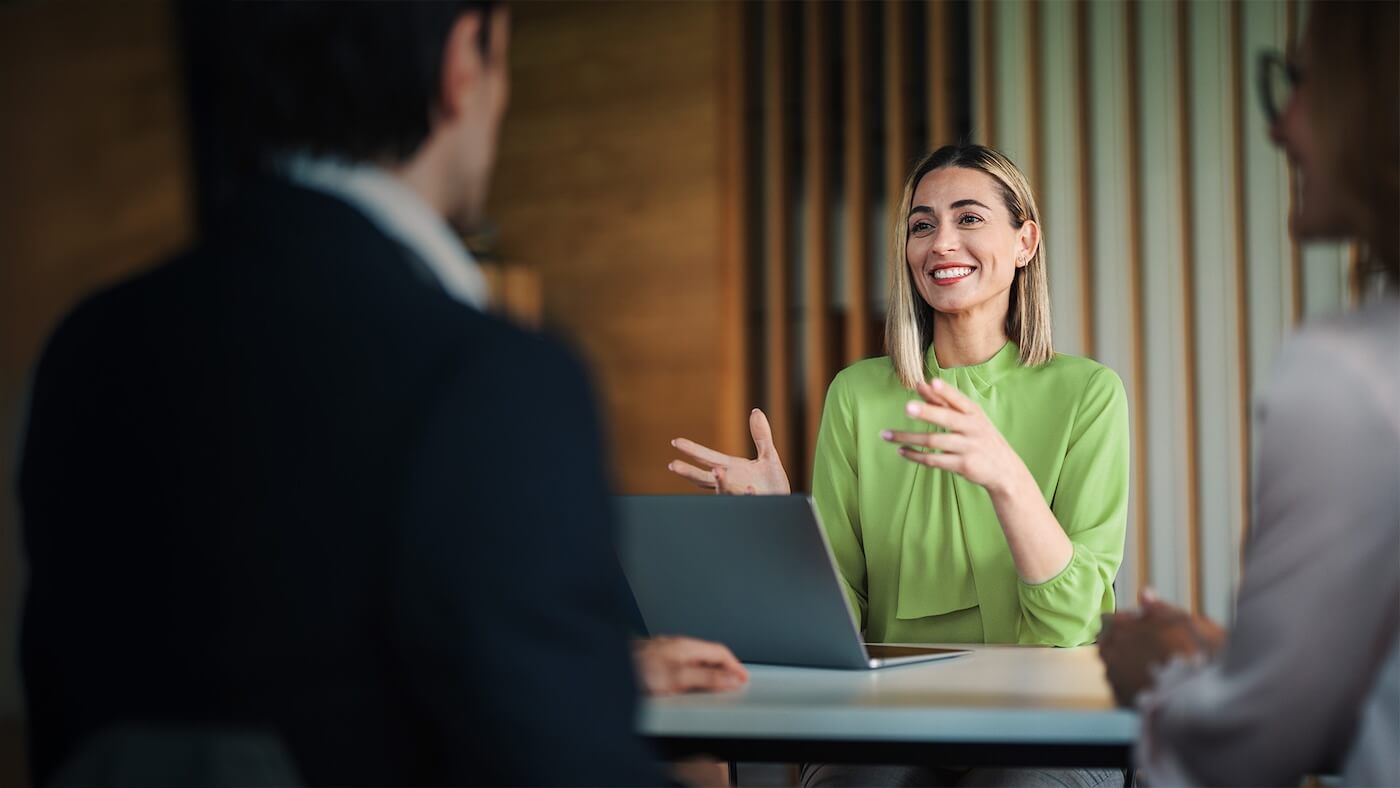 A woman at the desk with a laptop speaking with two professionals.
