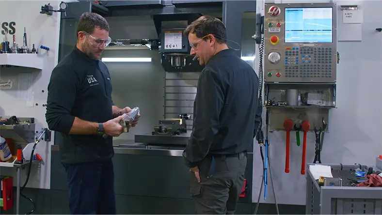 Mike Schultz and Noah Elliott discuss a material part in a design shop.