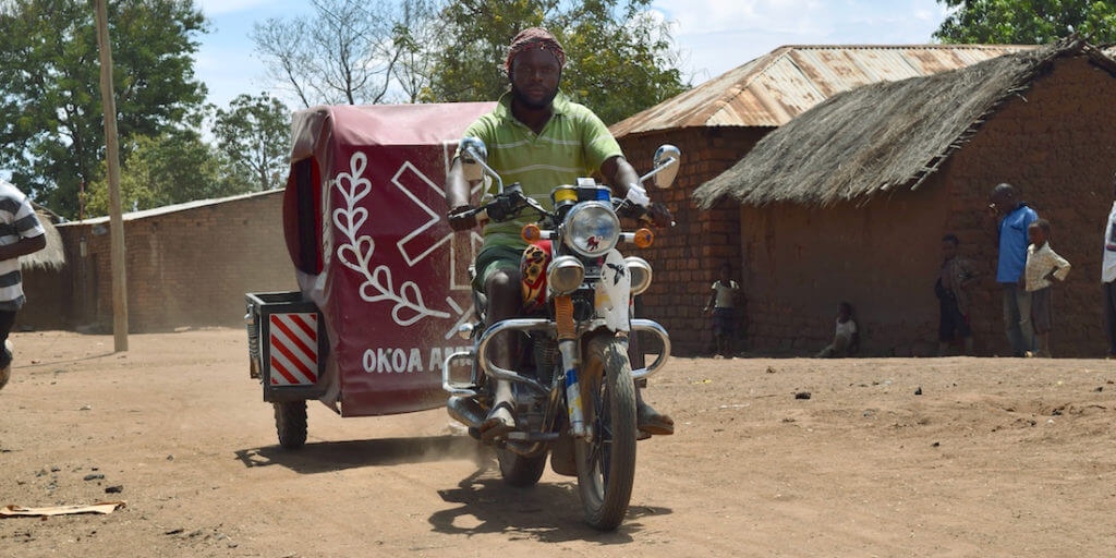 A man drives a motorcycle ambulance through a village in Tanzania