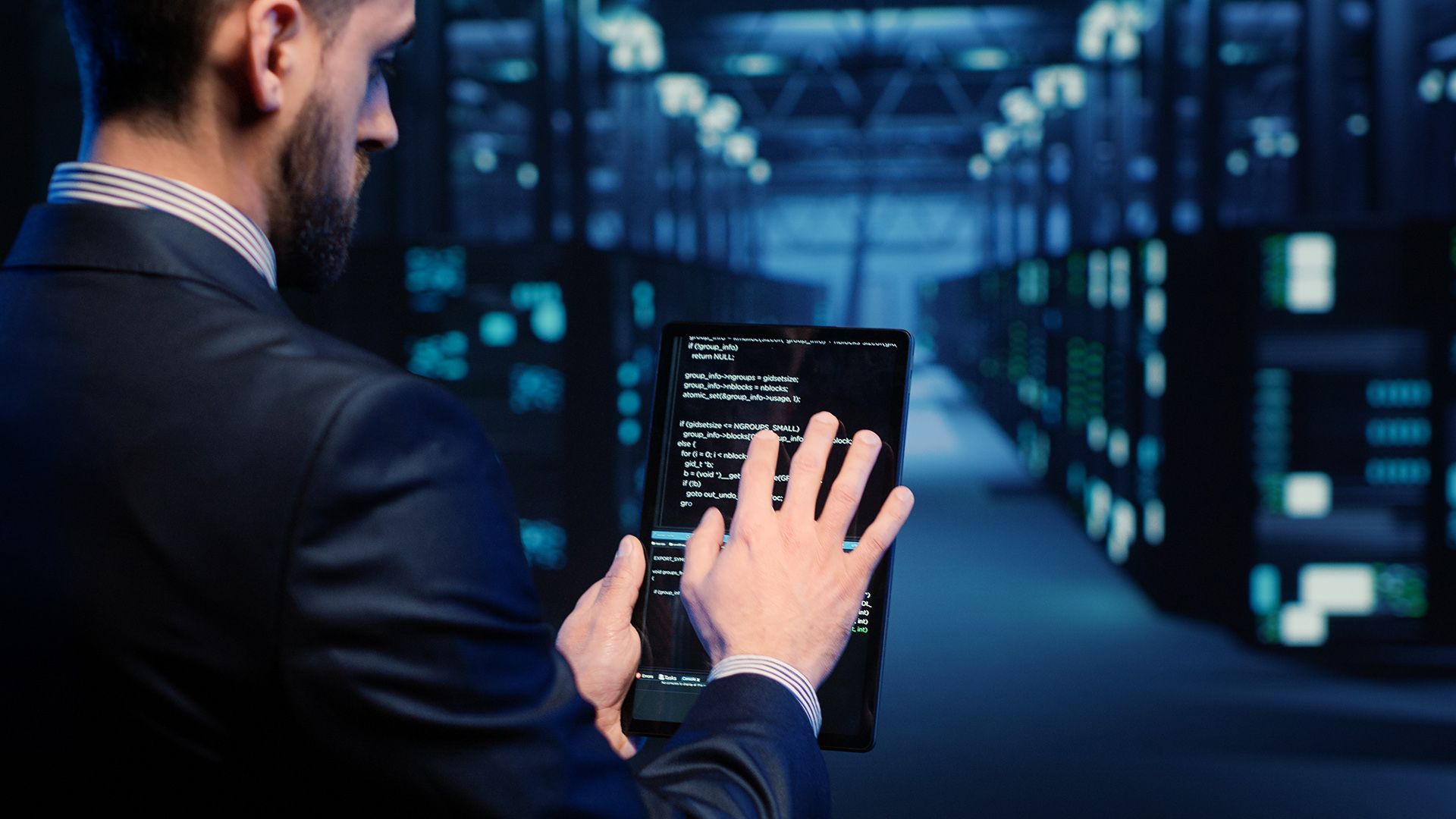 A man uses a tablet to monitor data in a server room.