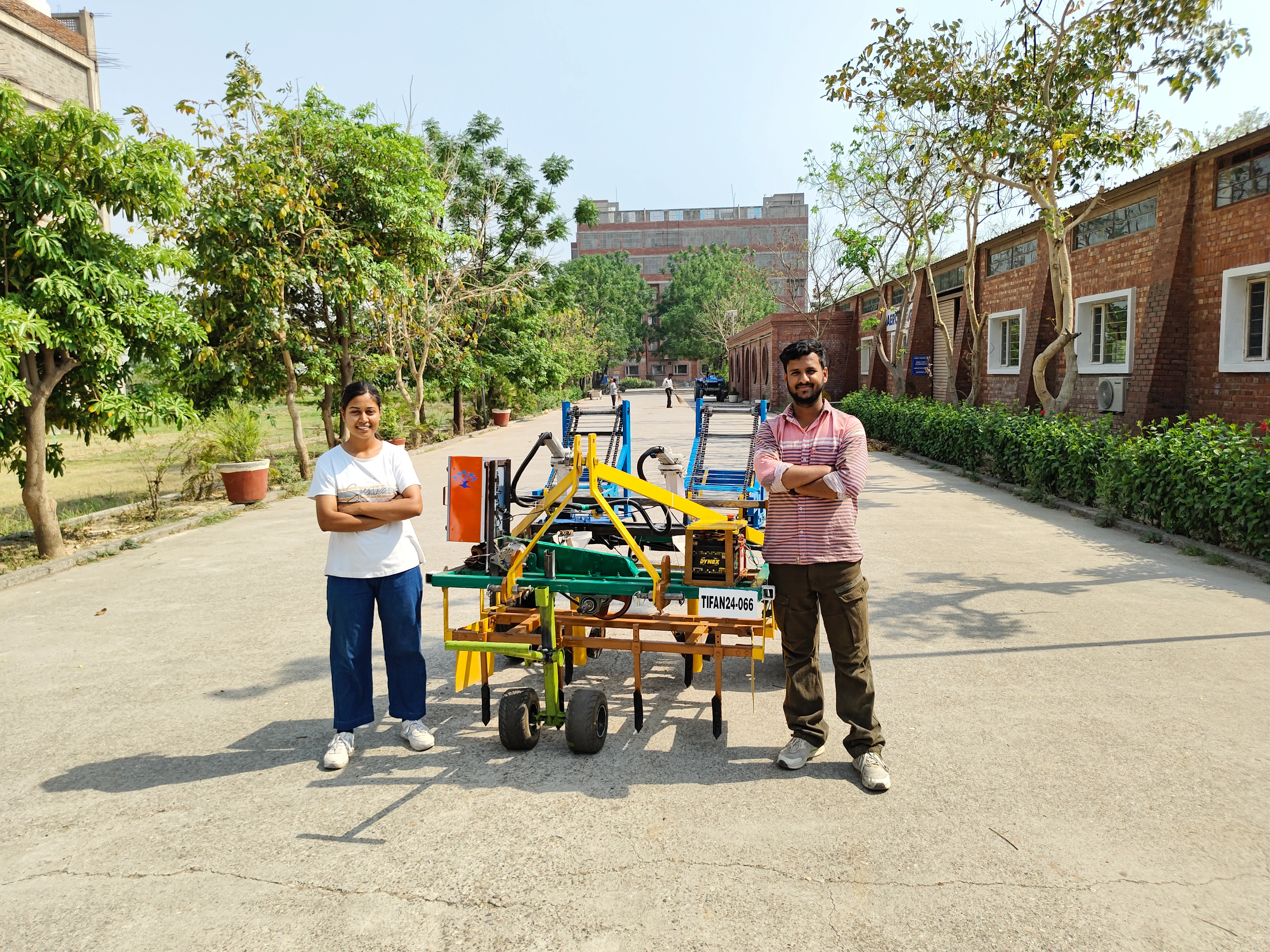 Two GNA University students standing with Automated Multi-Vegetable Transplanter