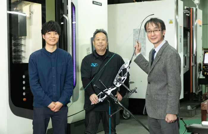 Three men pose with bow