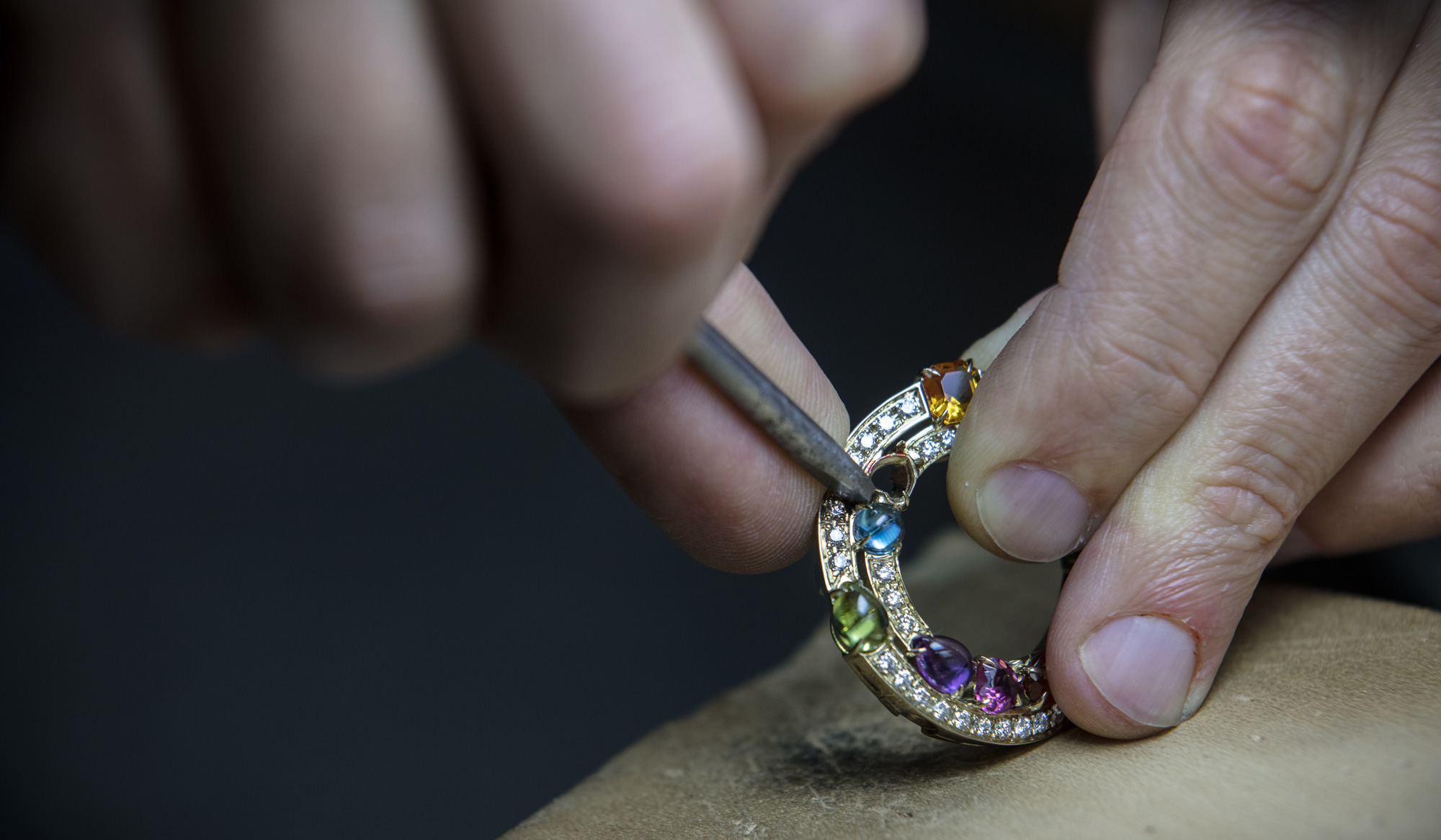 A Bulgari artist works on ring with multicolored gemstones.