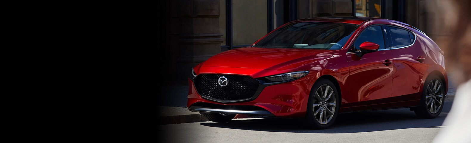 A red Mazda hatchback parked on a city street, showcasing its sleek design and modern styling.