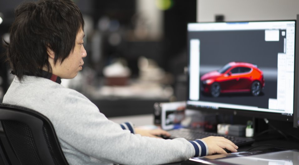 A person working on a computer, designing a red car model displayed on the monitor in a professional workspace.