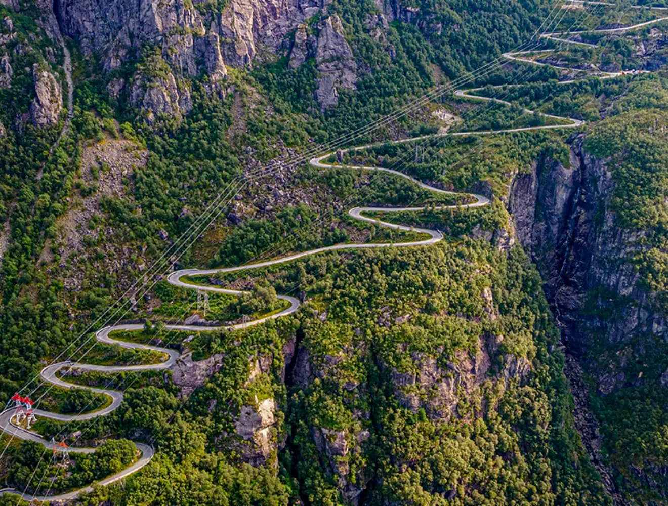 A curvy road winds up a cliffside, power lines run above the road.