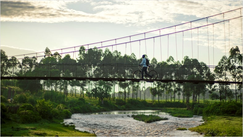 A side-angle view of a Bridges to Prosperity trail bridge on a mostly sunny day.