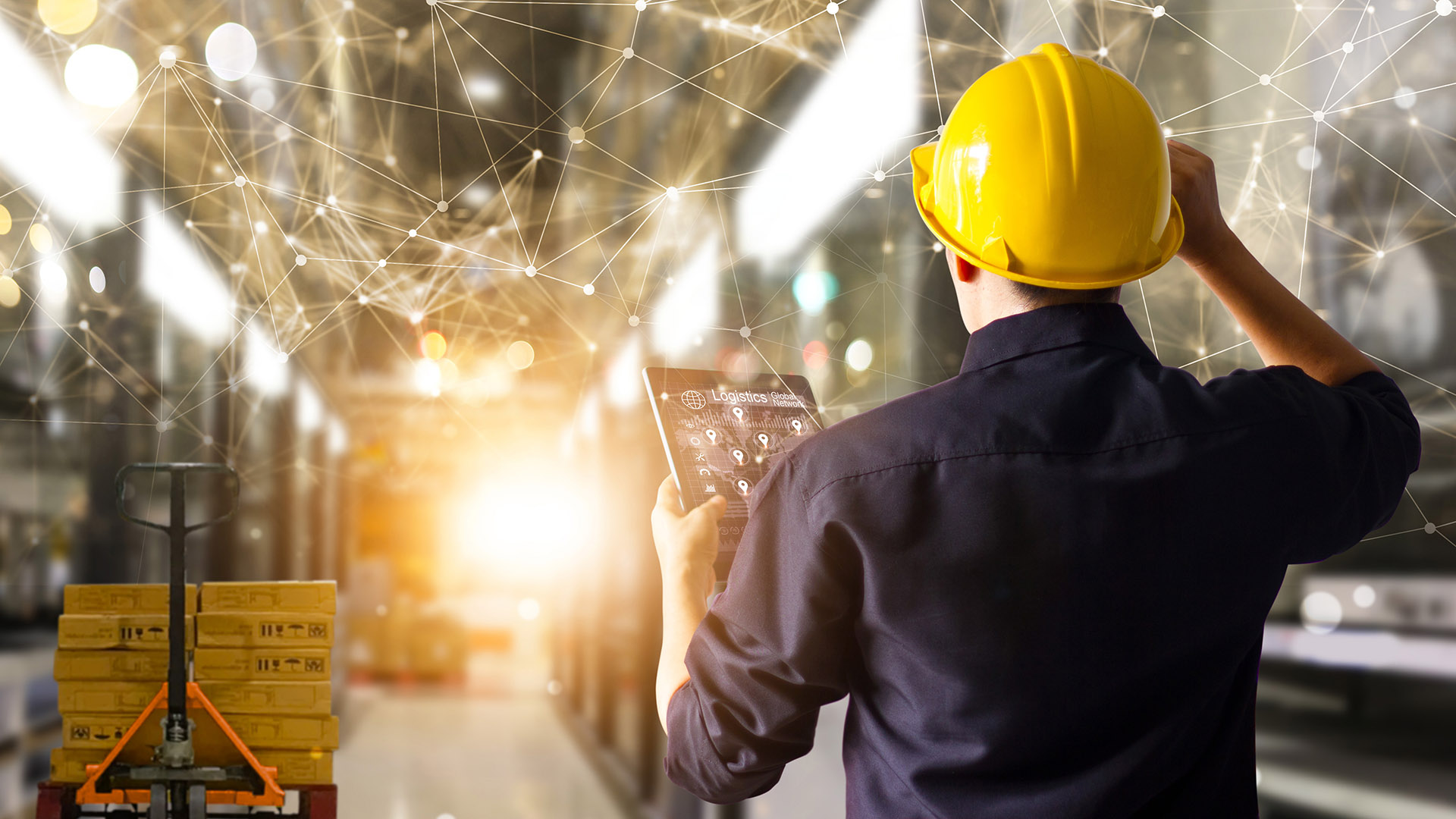 A man in a hard hat consults a tablet in a factory scene overlaid with graphics representing connectivity points.