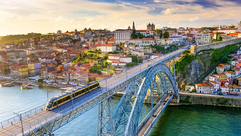 Light rail train crossing a bridge with a city in the background