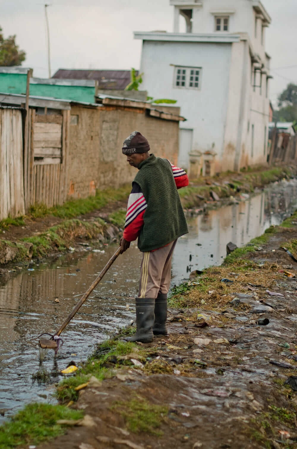 A man stands above an open trench full of dirty water