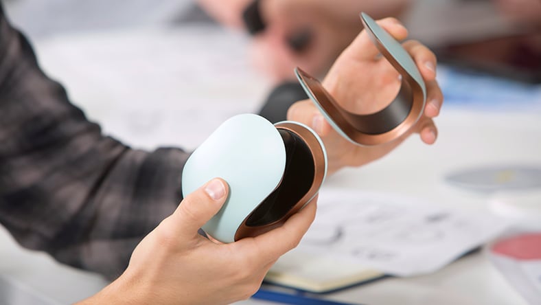 Person holding two plastic prototypes in front of desk with paperwork