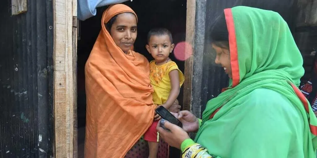 Woman holds child, while a second woman looks at phone