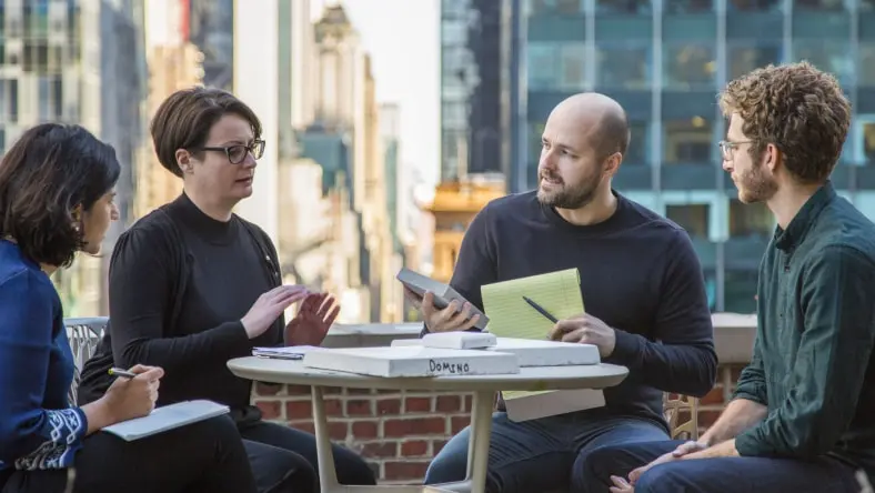 Image shows four professional people seated at a table outdoors discussing a project