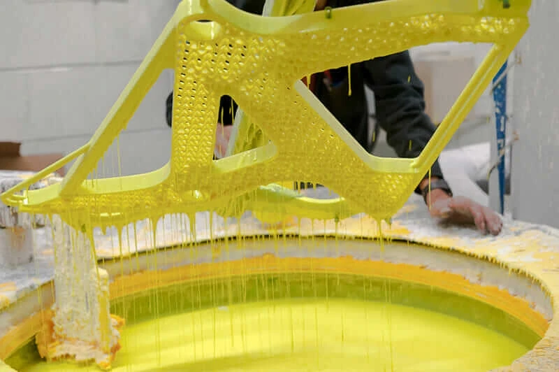 The mold pattern for an airplane seat frame is dipped in a yellow ceramic slurry.