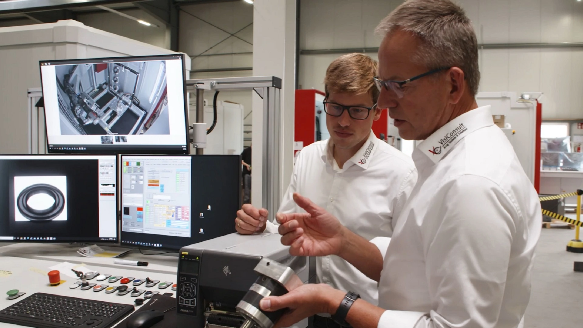 Two men examine a metal machine part next to the display screens of an X-ray inspection machine.