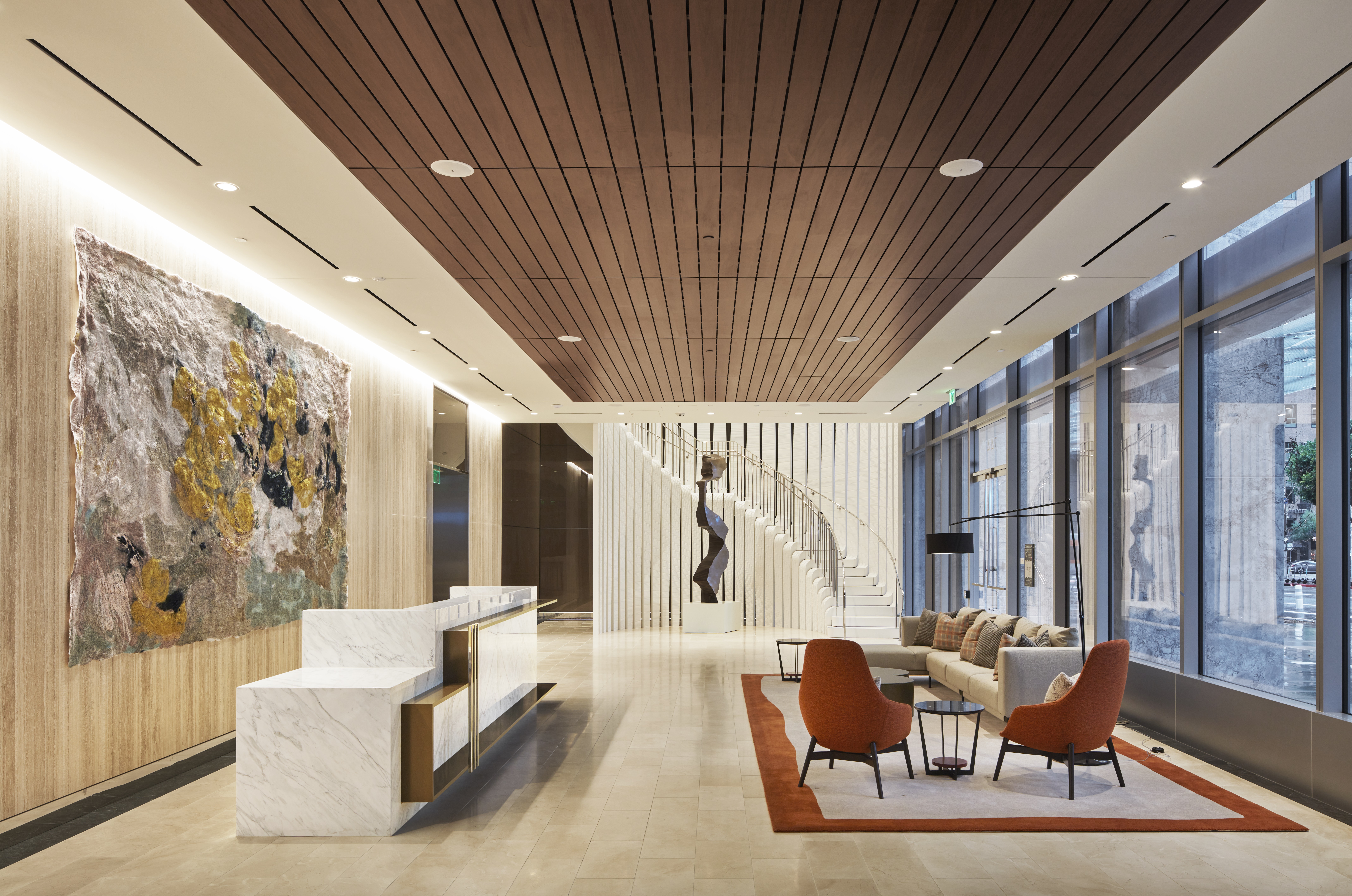 Interior with white reception desk, wood panel celing, sitting area with couch and two orange chairs, and spiral staircase