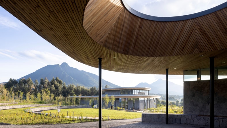 Ground view from the patio of one of the buildings of The Ellen DeGeneres Campus of the Dian Fossey Gorilla Fund in Rwanda. Foreground: Stone patio ground with curved, wood-paneled roof with large, round opening in the top, supported by thin black poles.