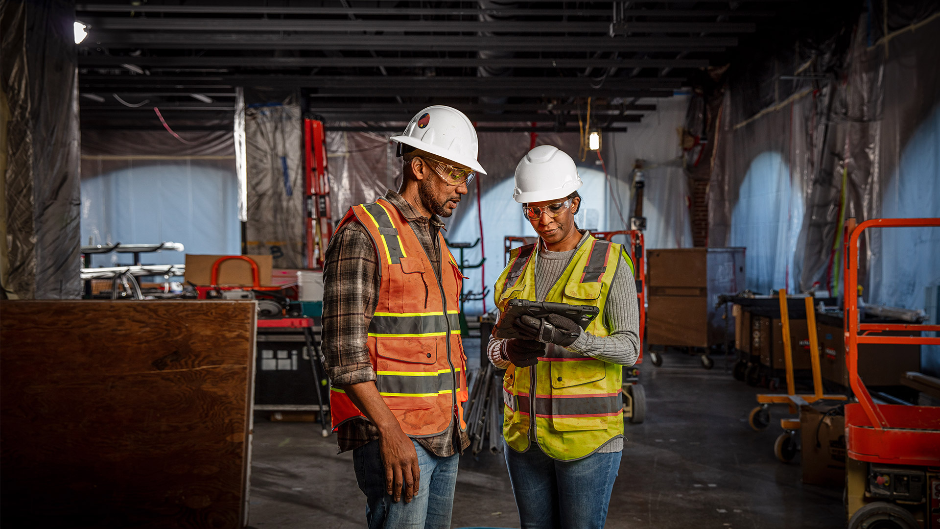 Construction workers in safety gear reviewing information on a tablet inside a job site under renovation.