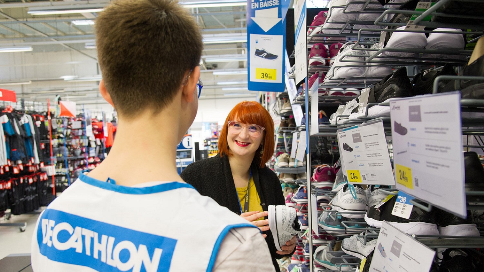 Two Decathlon employees organize a rack with multiple shoe selections.