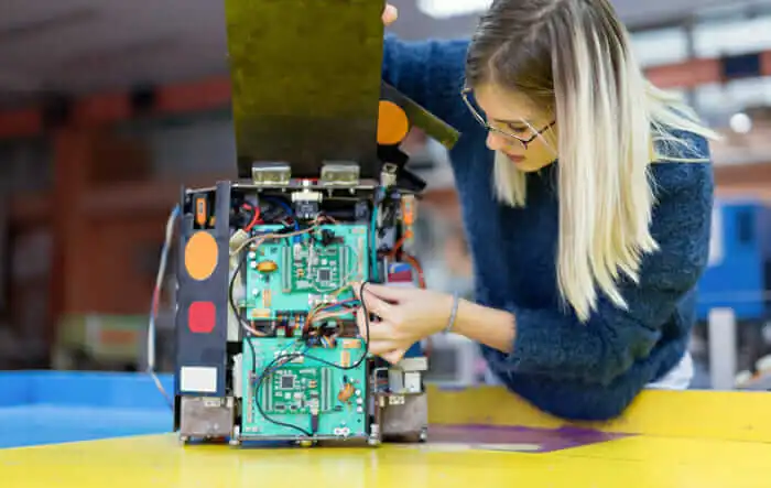 An employee on manufacturing floor works on circuit board of artificial-intelligence-enabled device.