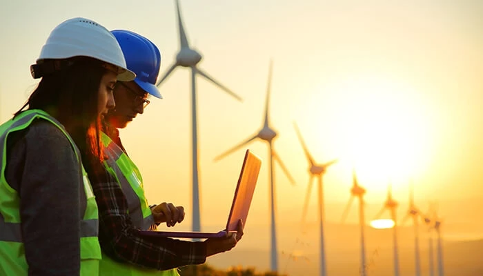Workers look at laptop in wind turbine field