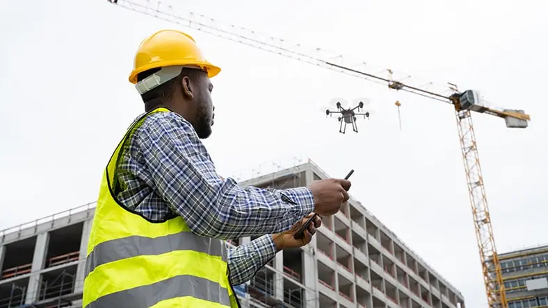 A construction worker in a hard hat uses a surveying drone.