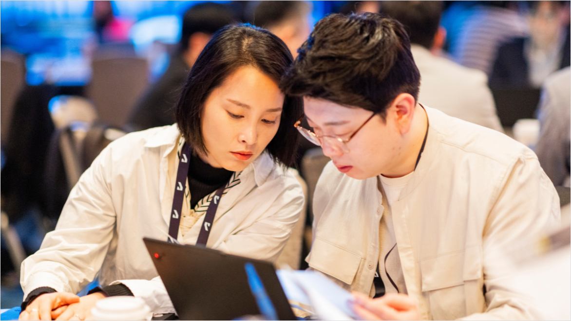 Two employees collaborate while reviewing information on a laptop in a meeting setting.