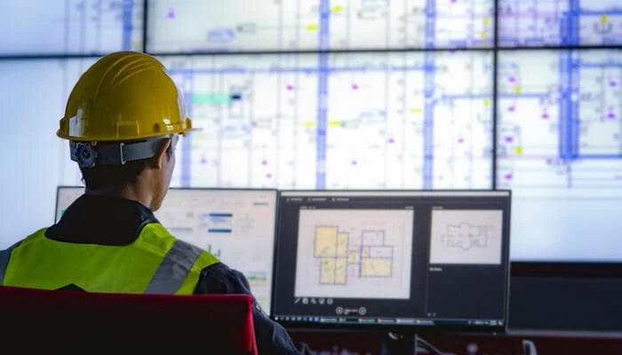 Man in construction hat looks at building plans on computer screen