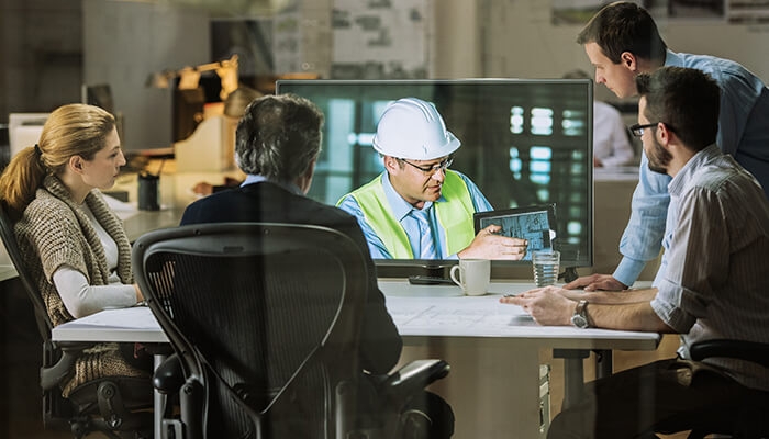 a group of coworkers collaborating around a computer screen, which is showing a construction worker on a jobsite