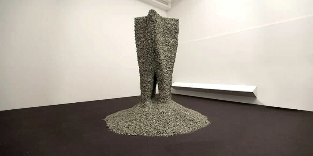 A large sculptural form, composed of small rocks held together with string, in a gallery setting.