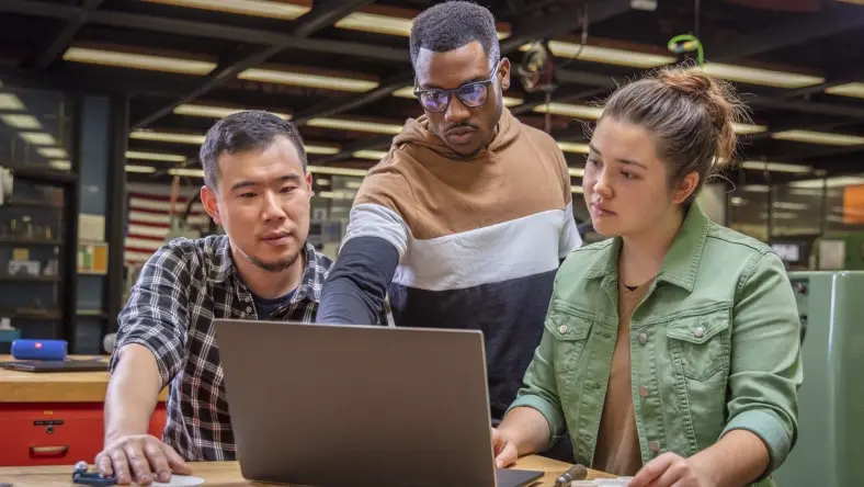 Image shows three people looking at a laptop together