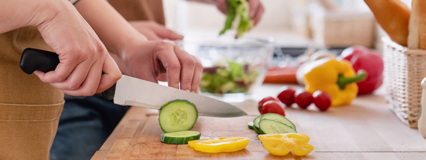 A person chopping cucumbers on a wooden cutting board.