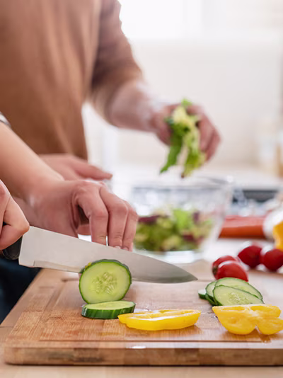 A person chopping cucumbers on a wooden cutting board.