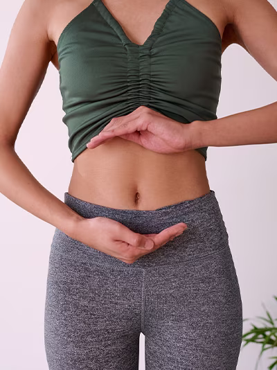 A woman standing with her hands resting on her lower abdomen.