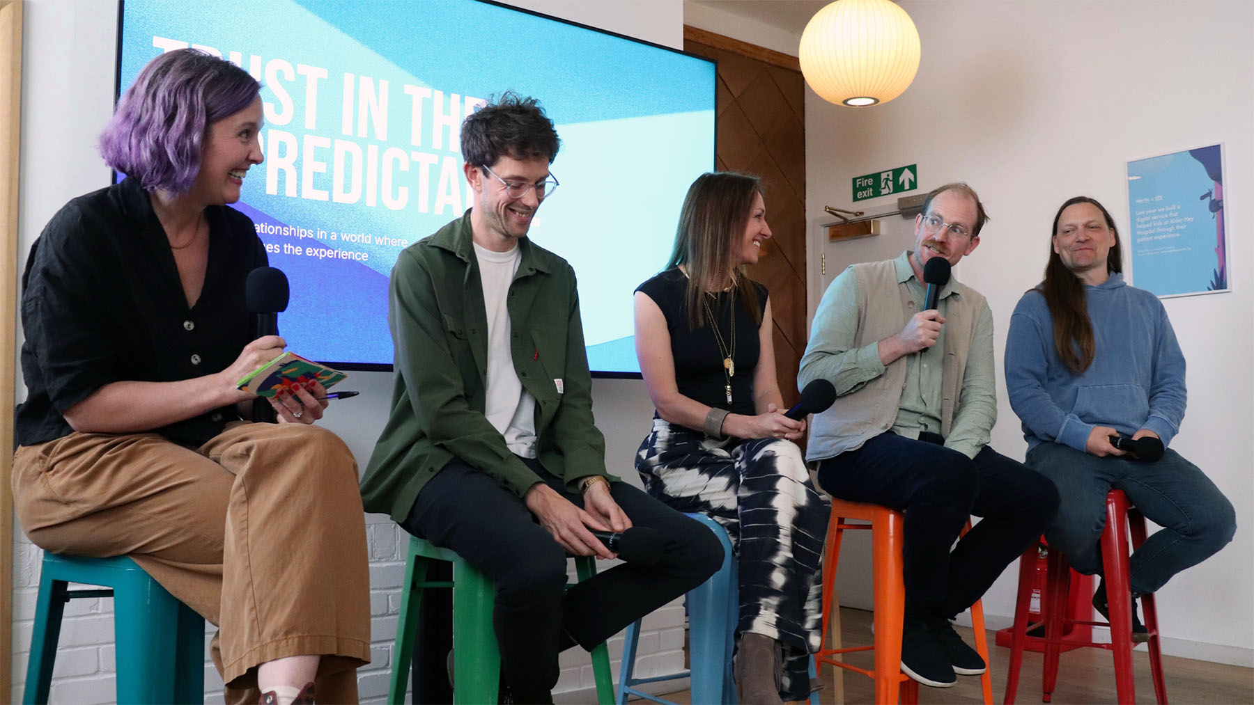 Five panellists sitting on chairs with ‘Trust in the unpredictable’ on the screen behind them.