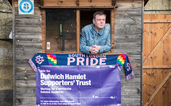 A member of the Dulwich Hamlet Supporters' Trust standing next to a 'South London Pride' scarf