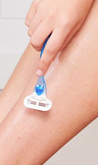 Hand hält Gillette Venus Oceana Rasierer über dem linken Bein