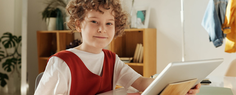 child looking at the camera smiling holding a tablet