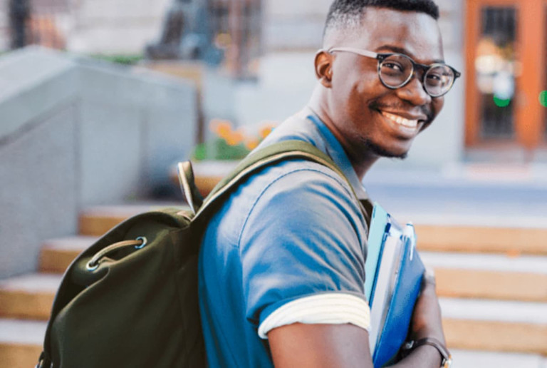 man with backpack holding books and smiling