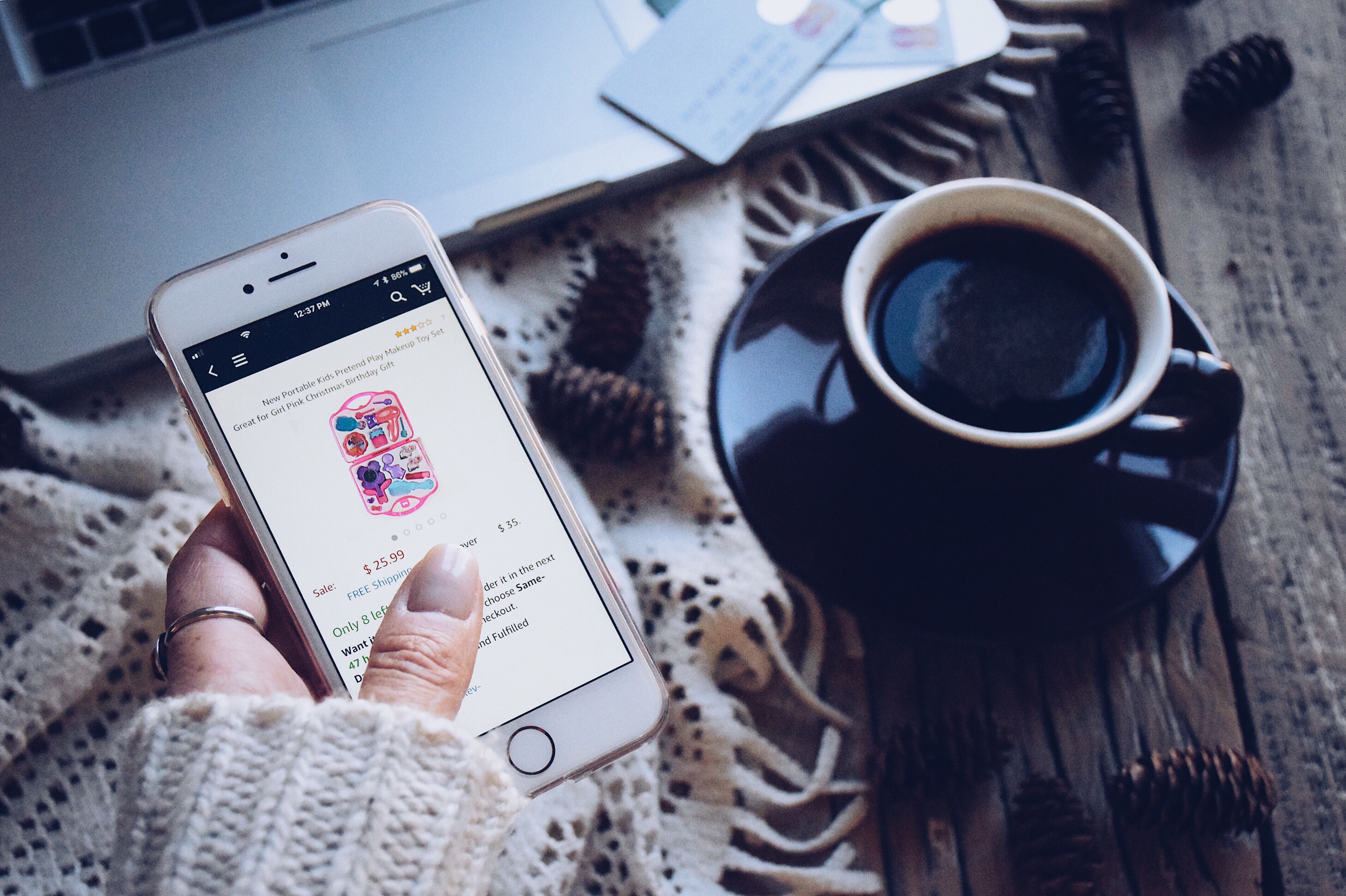 woman-is-shopping-for-girl-toys-on-a-mobile-phone-there-s-a-coffee-cup-pine-cones-laptop-credit-and t20 oo9JxR