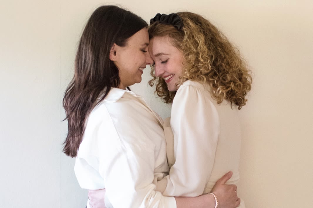 TWO GIRLS HUGGING. BOTH WEARING WHITE SHIRTS